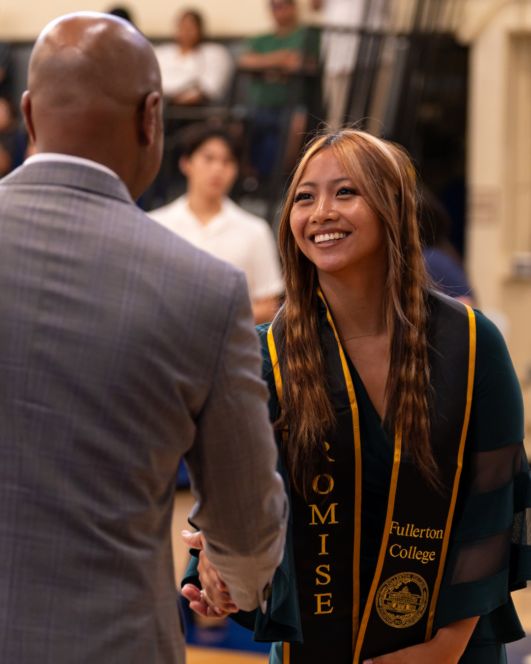 Student wearing a black "Promise" sash with gold embroidery shaking the NOCCCD Chancellors' hand.