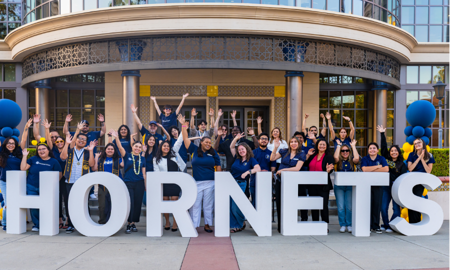 Staff celebrate at the Transfer Celebration in front of the Library with large white letters, detailing 'Hornets'.