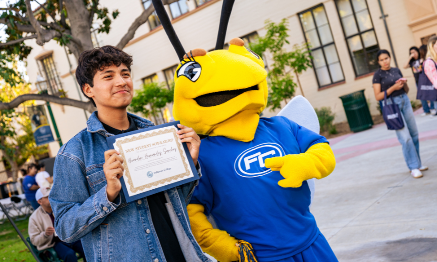 A student poses with Buzzy, holding up a certificate.