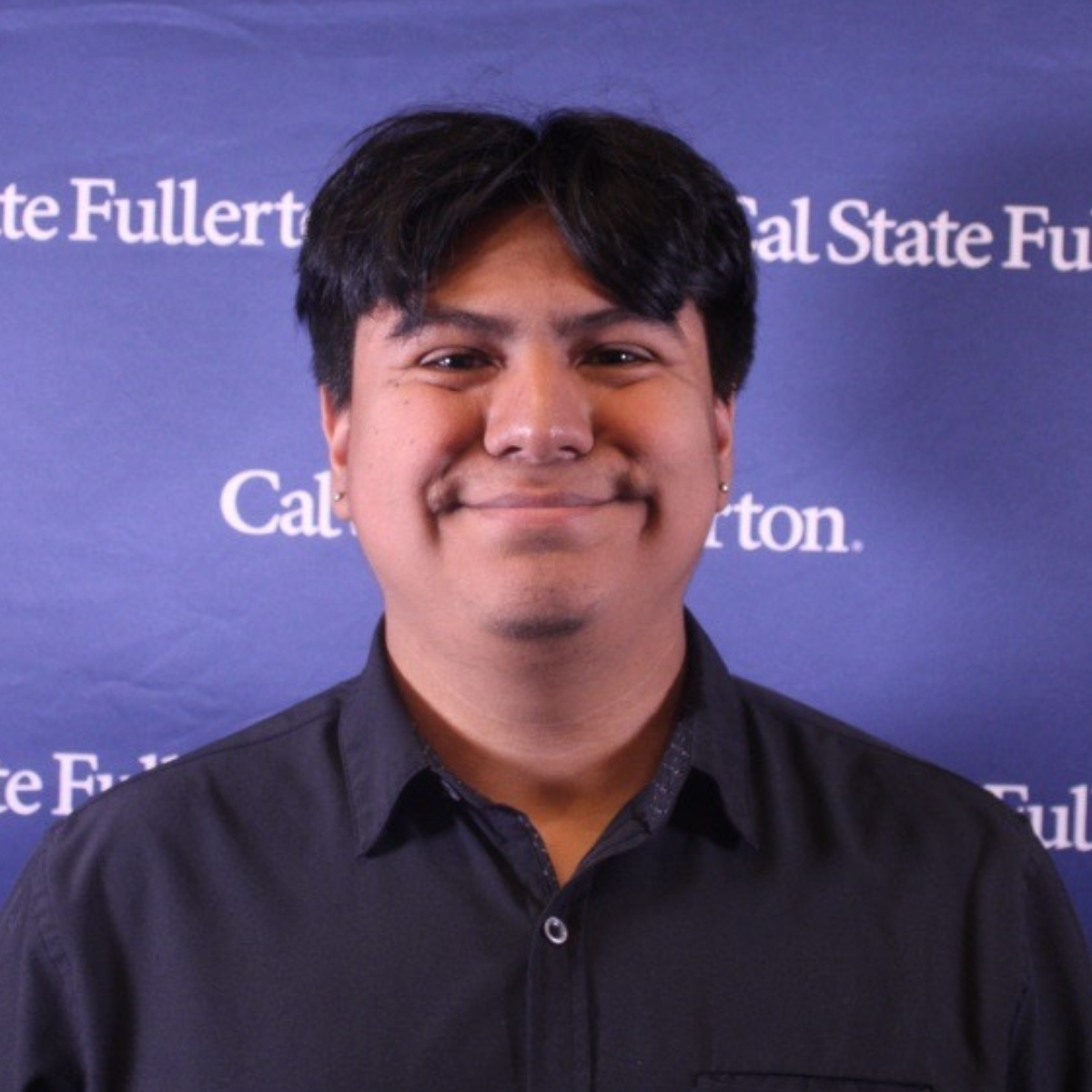 Photo of Brian wearing a black polo and standing in front of a blue CSUF backdrop